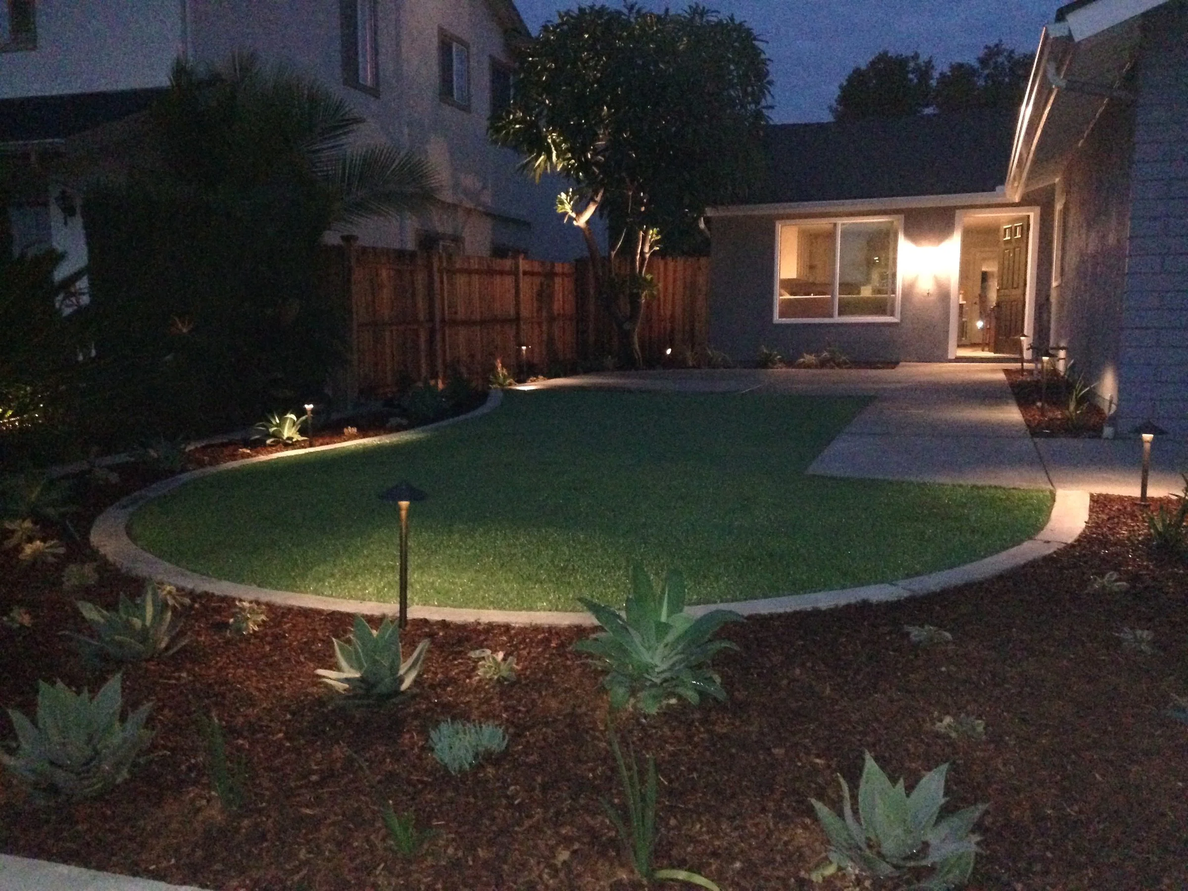 Backyard at dusk with a curved lawn and landscape lighting